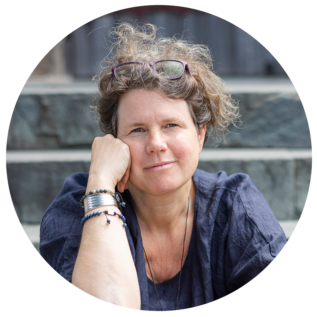 207 Eine Frau mit lockigem Haar, einer Brille auf dem Kopf und einem dunklen Hemd sitzt auf steinernen Stufen, stützt ihr Gesicht auf ihre Hand und lächelt leicht. Sie trägt Armbänder und wirkt entspannt und nachdenklich - ein ruhiger Moment der we:transform.