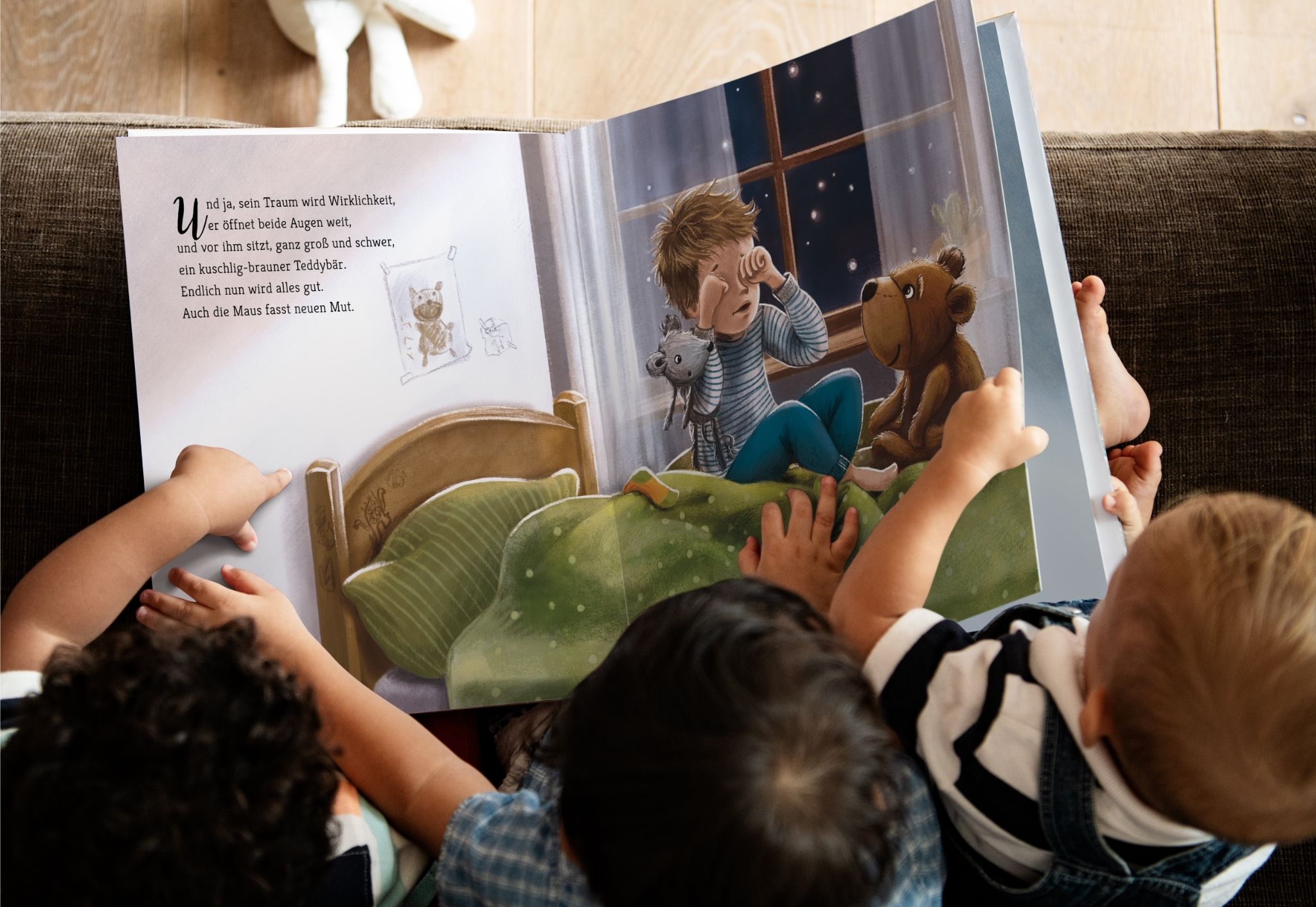 Drei kleine Kinder sitzen zusammen auf einer Couch und lesen ein großformatiges Bilderbuch von Patrick Beranek, das auf einer Seite aufgeschlagen ist, die einen Jungen mit Stofftieren im Bett zeigt. Zwei Kinder zeigen auf das Buch und sind in die Geschichte vertieft.