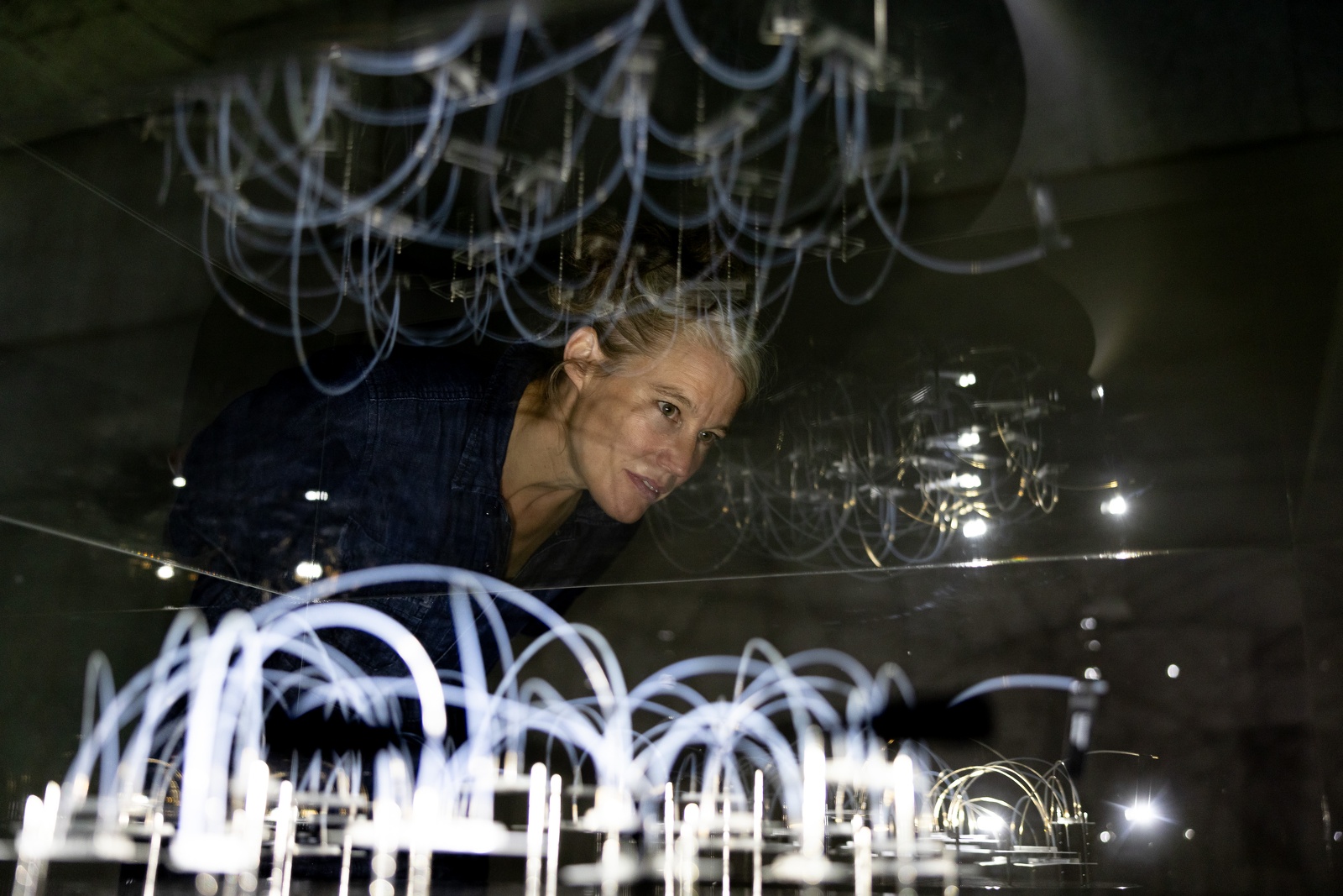 Eine Frau auf dem Forward Festival starrt nachdenklich auf ein leuchtendes Licht, fasziniert von der kreativen Atmosphäre um sie herum.