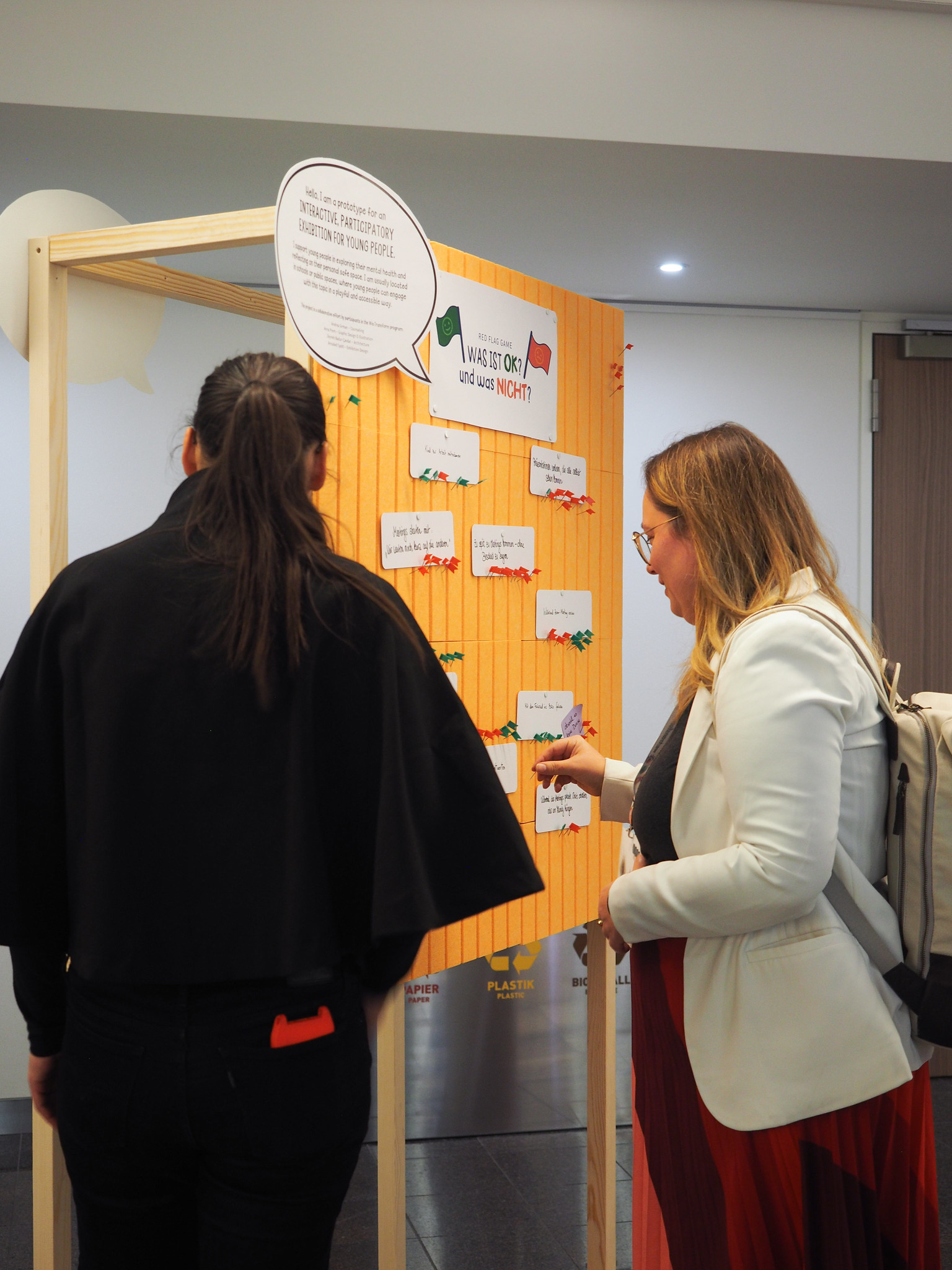 Zwei Frauen stehen vor einer Schautafel des CIMIx 2026 mit Fragen und Karten und diskutieren über den Inhalt. Eine Frau zeigt auf eine Karte, während die andere zusieht. Die Tafel ist mit Sprechblasen und bunten Notizen versehen.