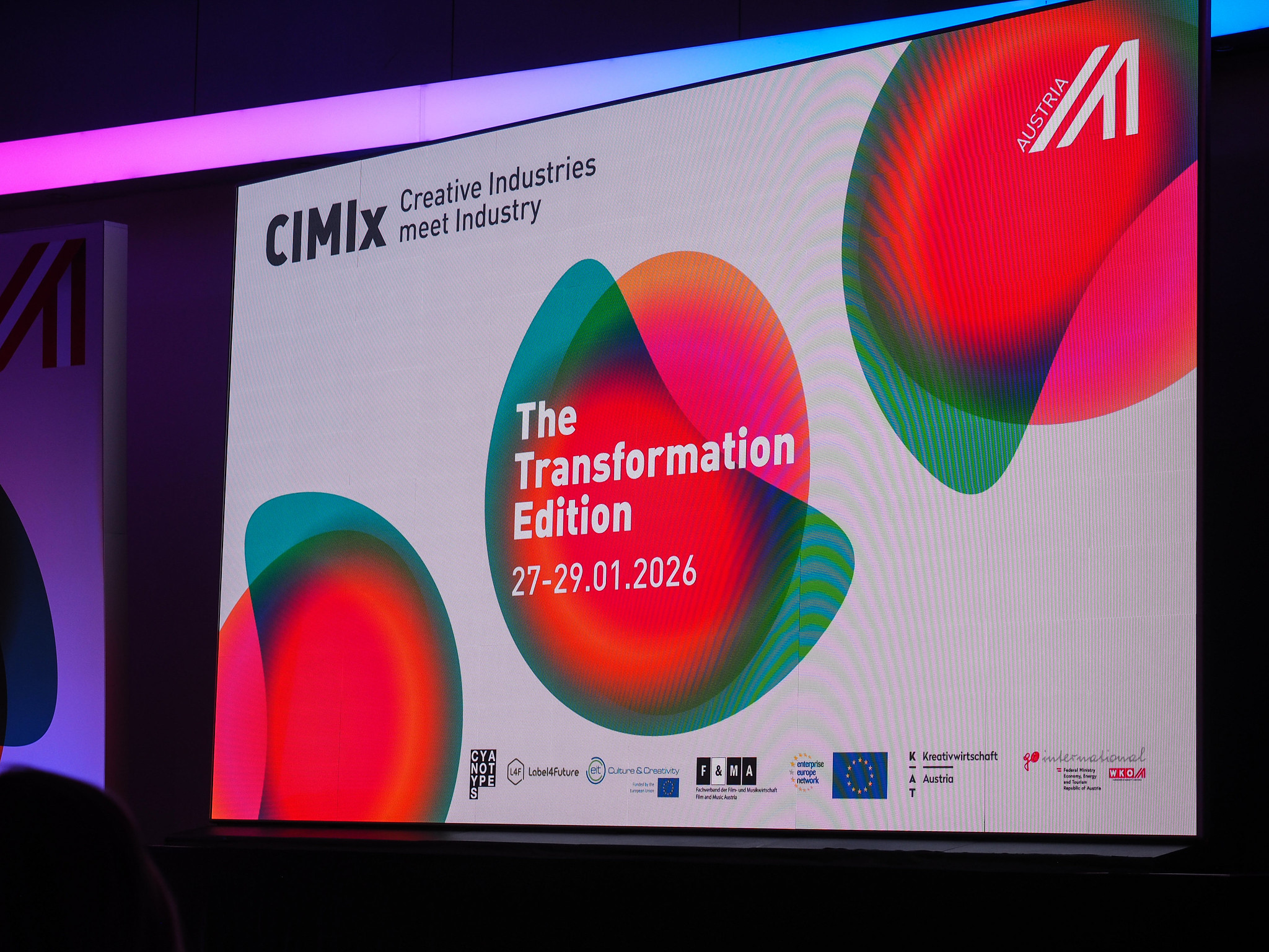 Ein großer Bildschirm zeigt das CIMIx-Veranstaltungslogo mit bunten abstrakten Formen und der Aufschrift: The Transformation Edition, Connecting the dots 2026, 27-29.01.2026. Am unteren Rand sind verschiedene Sponsorenlogos und ein QR-Code zu sehen.