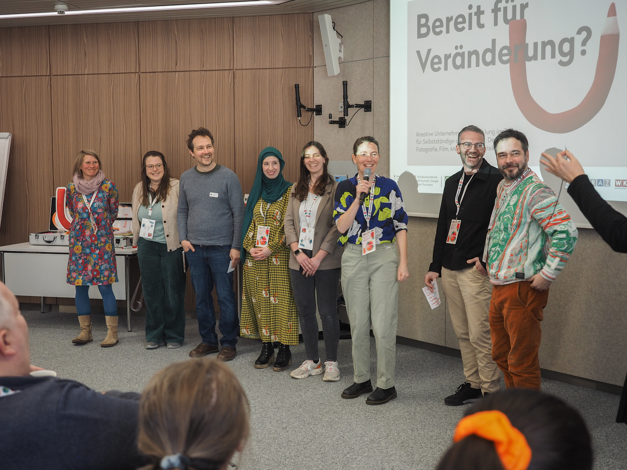 Eine Gruppe von acht Personen steht lächelnd vor einem Publikum in einem Konferenzraum. Hinter ihnen zeigt ein Bildschirm den deutschen Satz "Bereit für Veränderung?" auf der Veranstaltung CIMIx 2026.