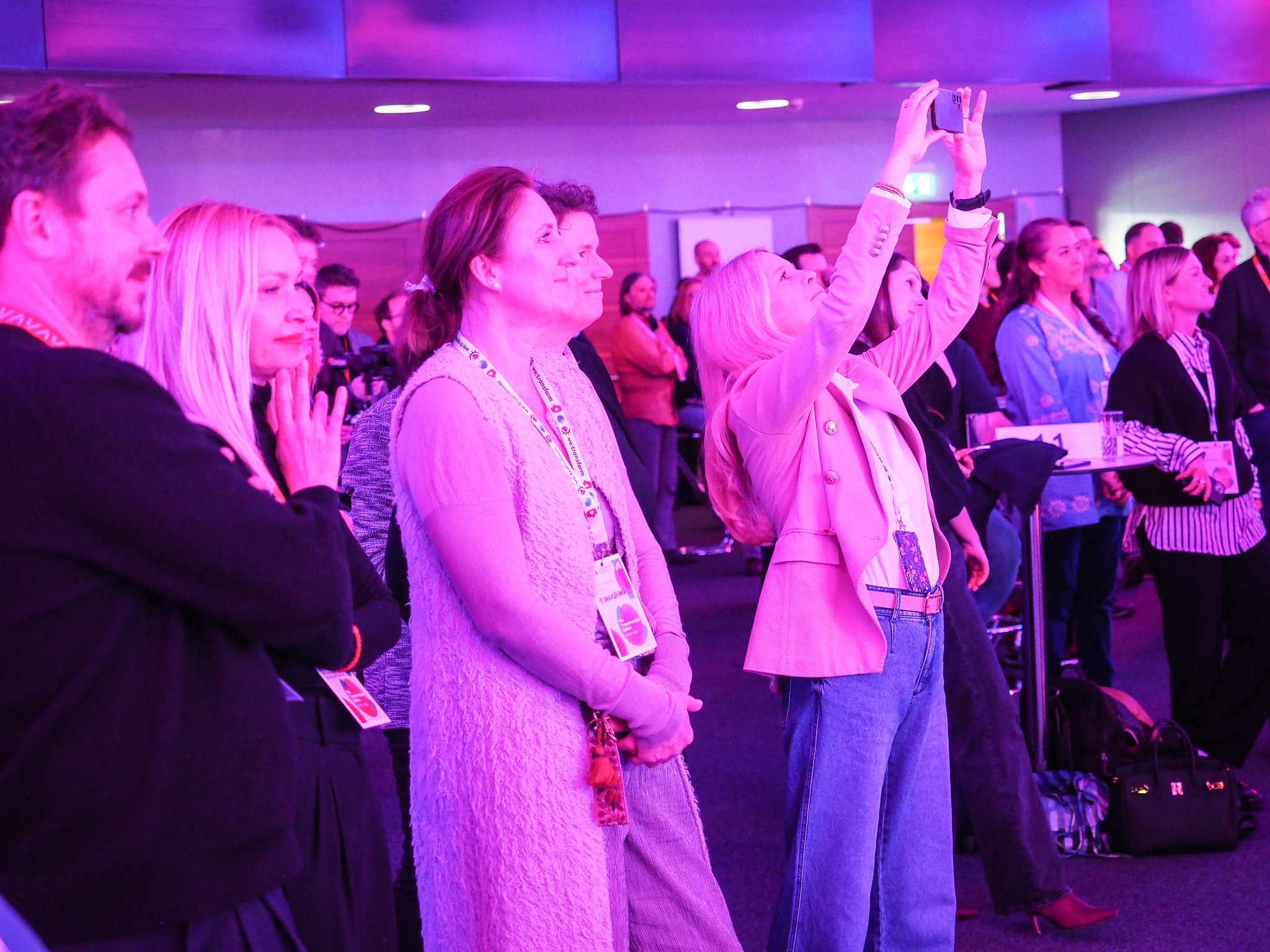 Eine Gruppe von Menschen steht in einem Innenraum des CIMIx 2026 unter violettem Licht und beobachtet eine Veranstaltung. Eine Frau im Vordergrund hält ein Telefon hoch, um ein Foto oder ein Video aufzunehmen. Die meisten blicken nach vorne und wirken engagiert.