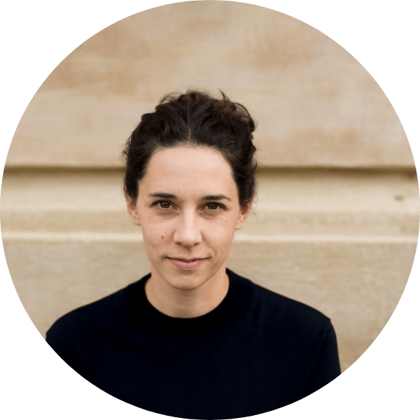 207 Eine Person mit dunklem, zurückgebundenem Haar und schwarzem Oberteil blickt mit neutralem Blick in die Kamera. Der Hintergrund ist beige und leicht strukturiert. Das Bild ist mit einem kreisförmigen Ausschnitt gerahmt.