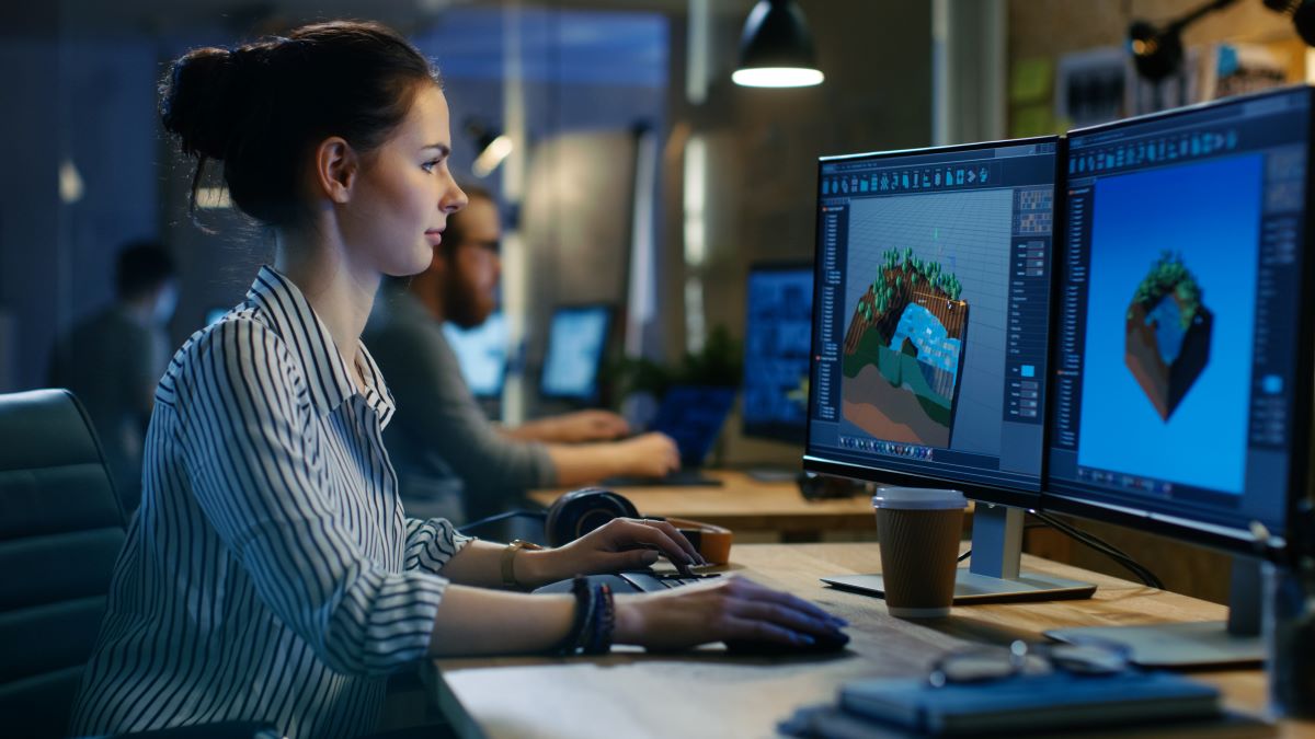 Eine Frau sitzt an einem Schreibtisch mit zwei Monitoren, auf denen 3D-Landschaftsmodelle zu sehen sind, und lässt sich zu neuen Spielideen inspirieren. Sie bedient Maus und Tastatur, neben ihr steht eine Kaffeetasse. Im Hintergrund arbeiten weitere Menschen an Computern in einem modernen Büro, das vom Geist des „PLAYING ART“ geprägt ist.