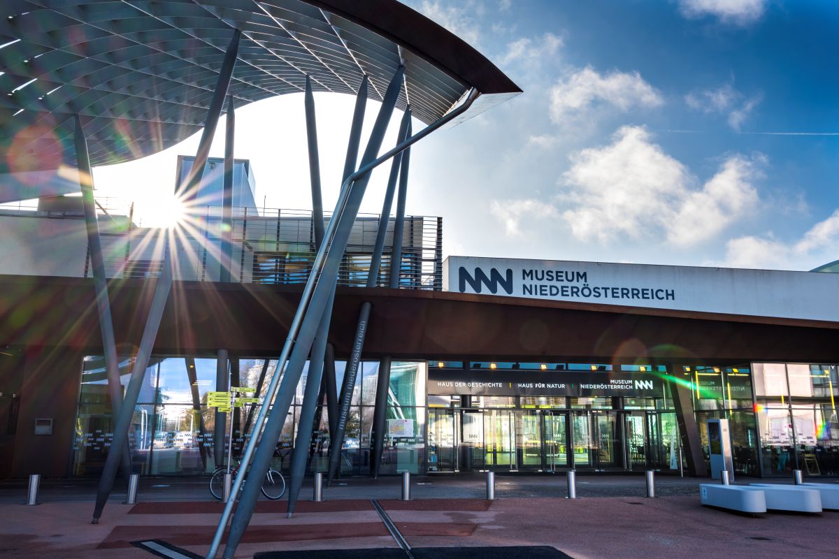 Der moderne Eingangsbereich aus Glas und Stahl des Museums Niederösterreich in Österreich, durch den das Sonnenlicht scheint, mit dem blauen Himmel im Hintergrund – ein Bild, das die lebendige Atmosphäre einfängt, die beim Medien,Tag 2026 gefeiert werden wird.