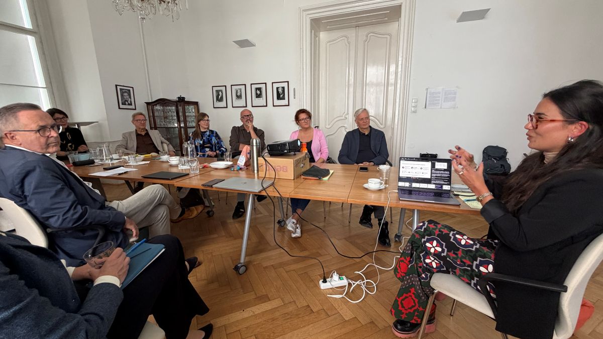 Magdalena Kim Novak gestikuliert, während sie mit einer Gruppe von Menschen, die um einen langen Konferenztisch sitzen, über die Zukunft spricht.